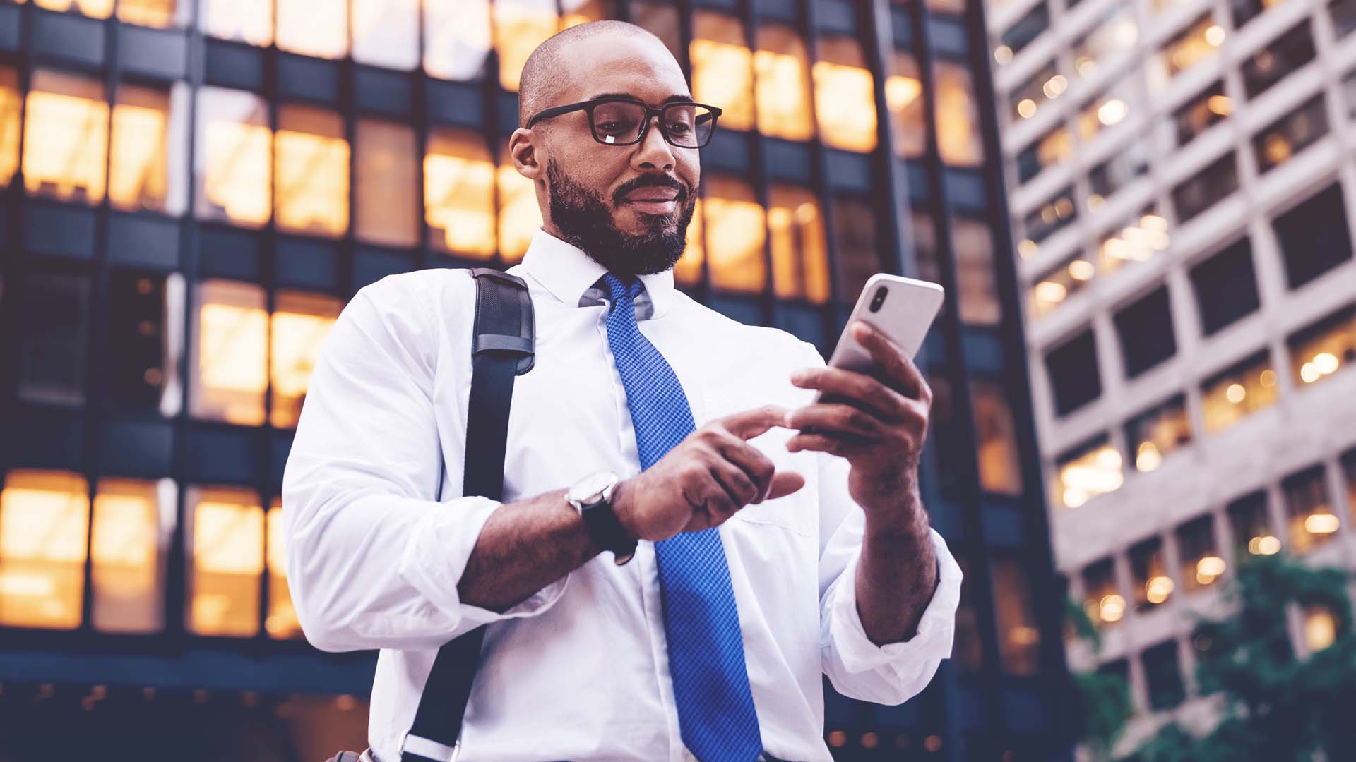 Professional man looking at his phone while outside among office buildings