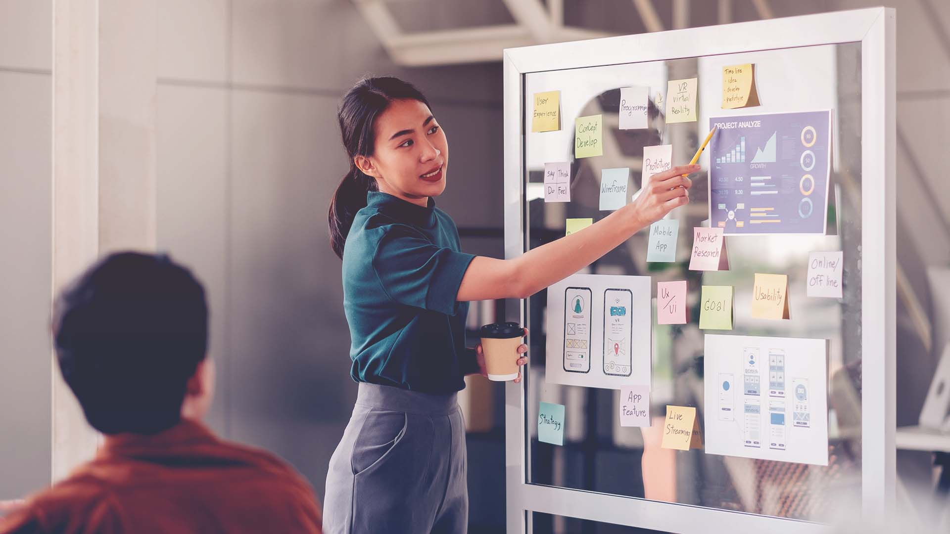 young professional woman standing at a board working through a process using post-its
