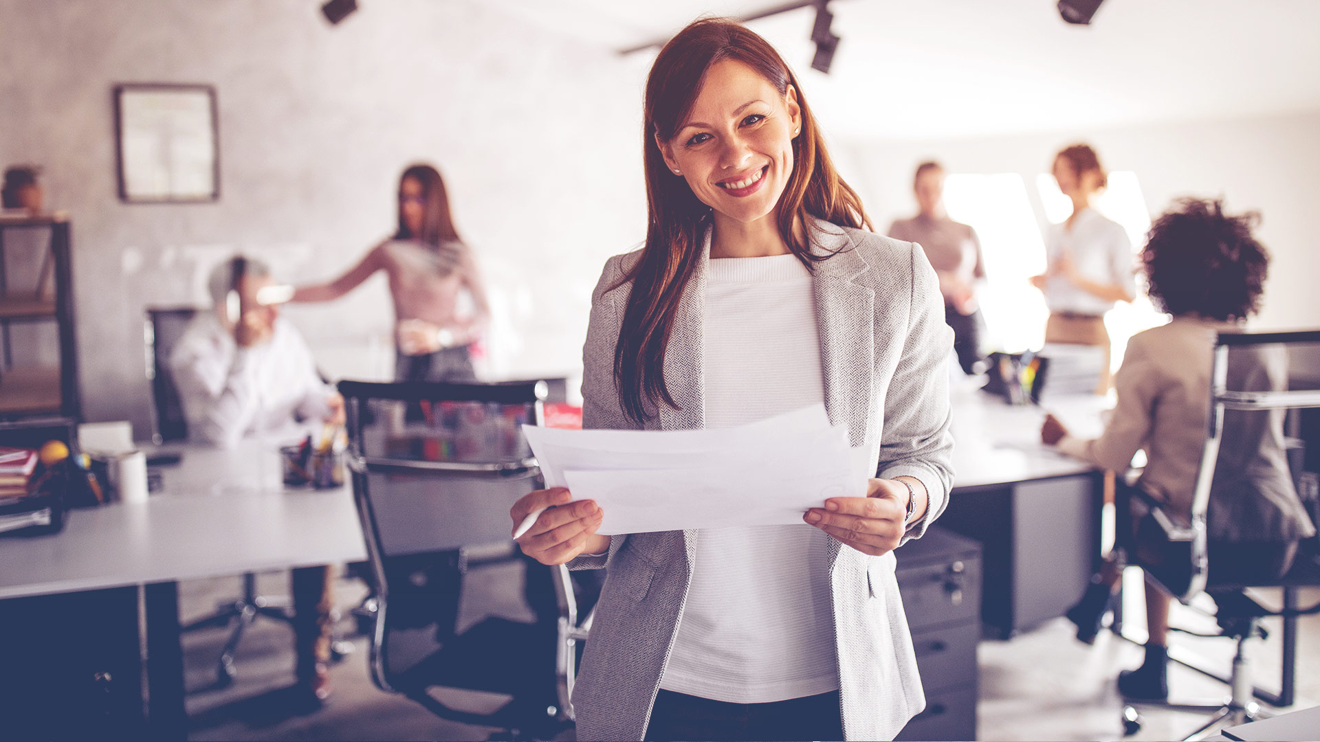 Smiling young professional woman in a conference room holding a pen & papers 