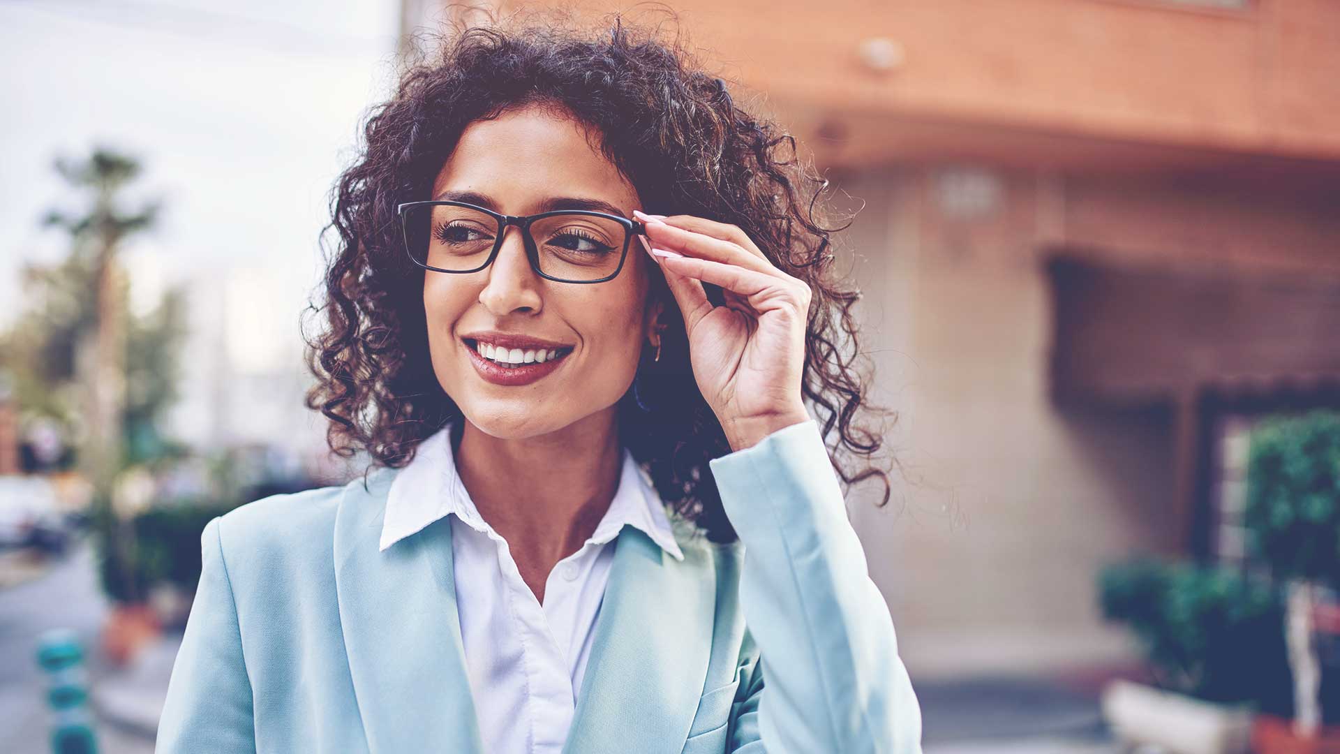 professional woman with curly hair adjusting her glasses