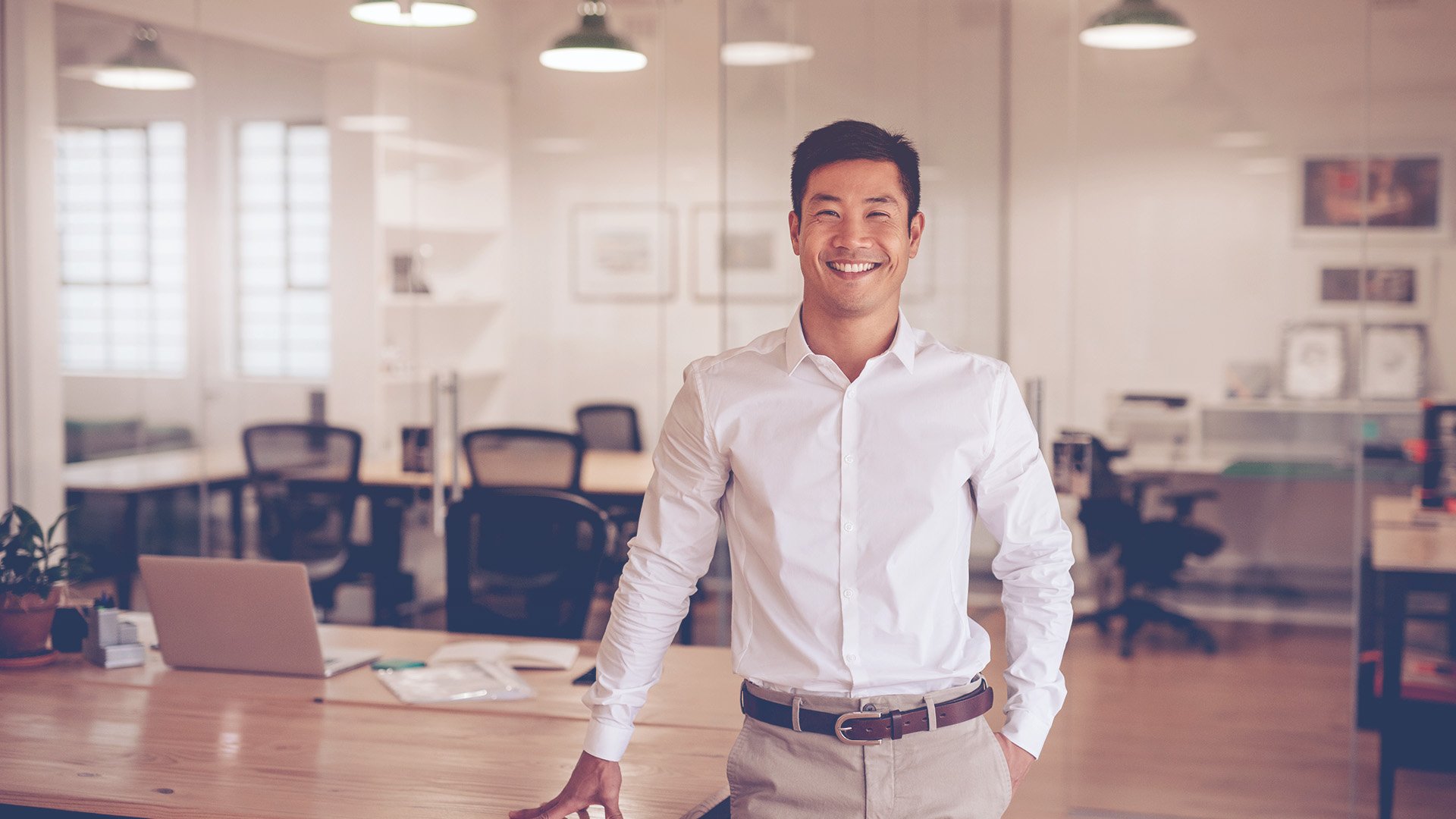 asian man in white button down shirt smiling at the camera inside an office building