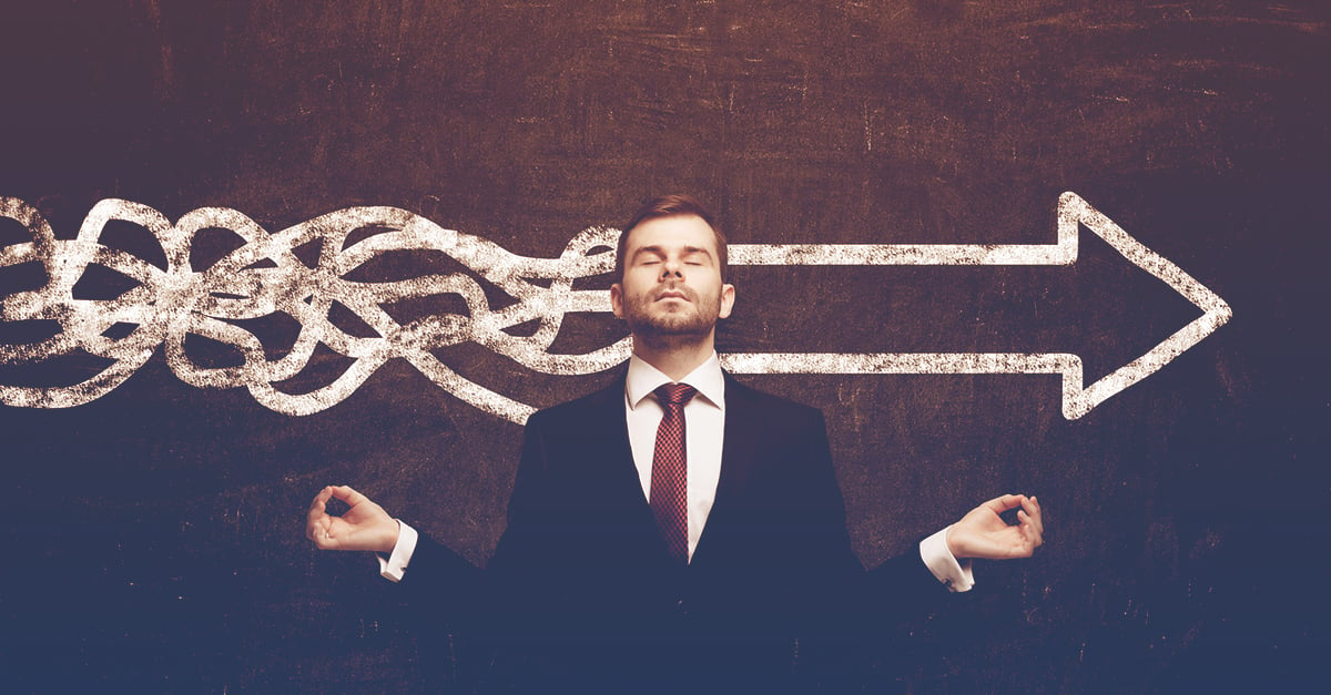 business professional meditating in front of chalkboard that has chaotic lines that transition to a smooth arrow